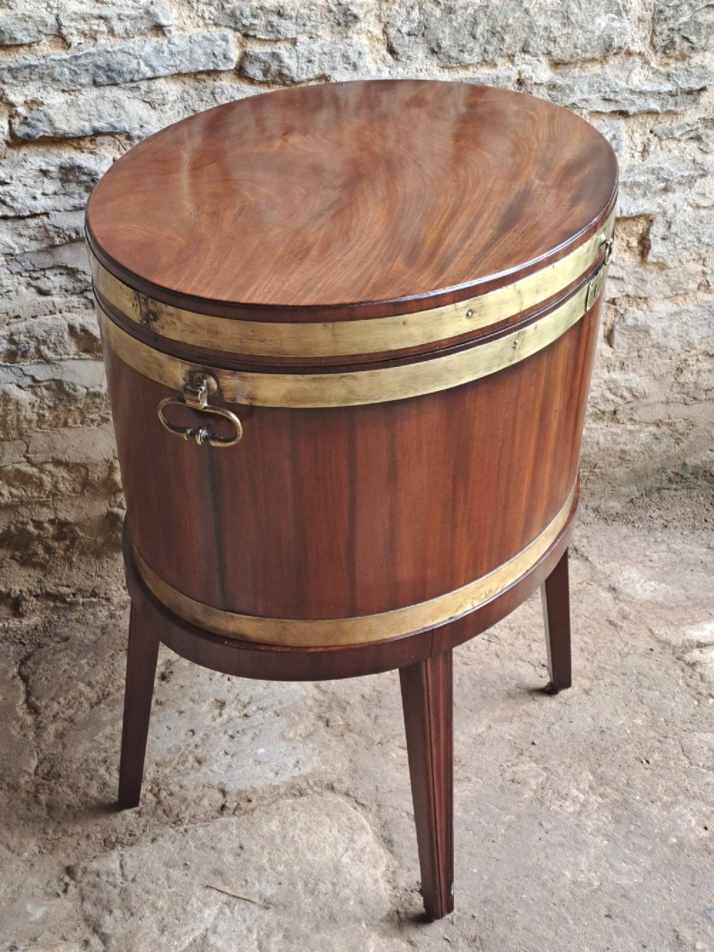 An 18th-century George III oval mahogany cellarette bound with brass straps and supported by four tapered legs. View IX