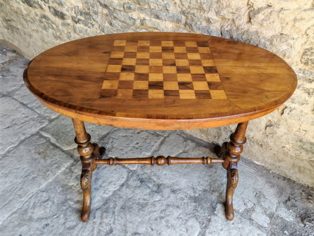 An oval walnut occasional table featuring an inlaid square chess board in the centre, supported by turned legs and a stretcher base.