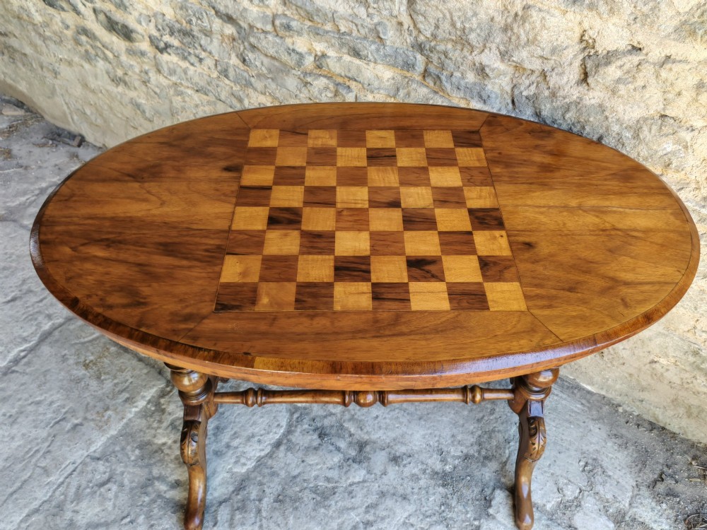 An oval walnut occasional table featuring an inlaid square chess board in the centre, supported by turned legs and a stretcher base. View II