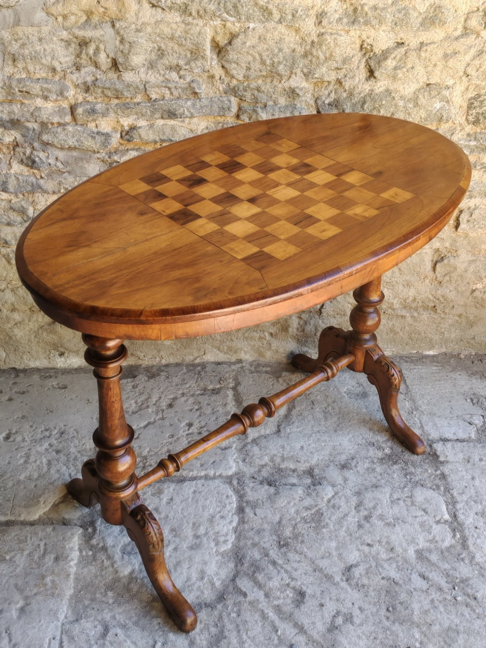 An oval walnut occasional table featuring an inlaid square chess board in the centre, supported by turned legs and a stretcher base. View III