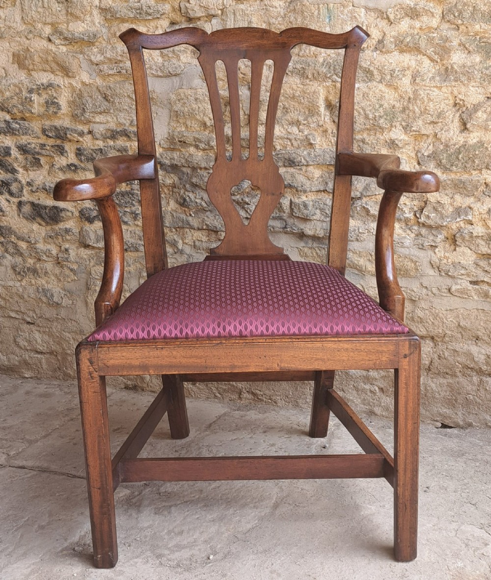 An 18th-century Irish walnut open armchair featuring a carved pierced splat, shaped armrests, an H-stretcher base, and a burgundy pattern upholstered seat.