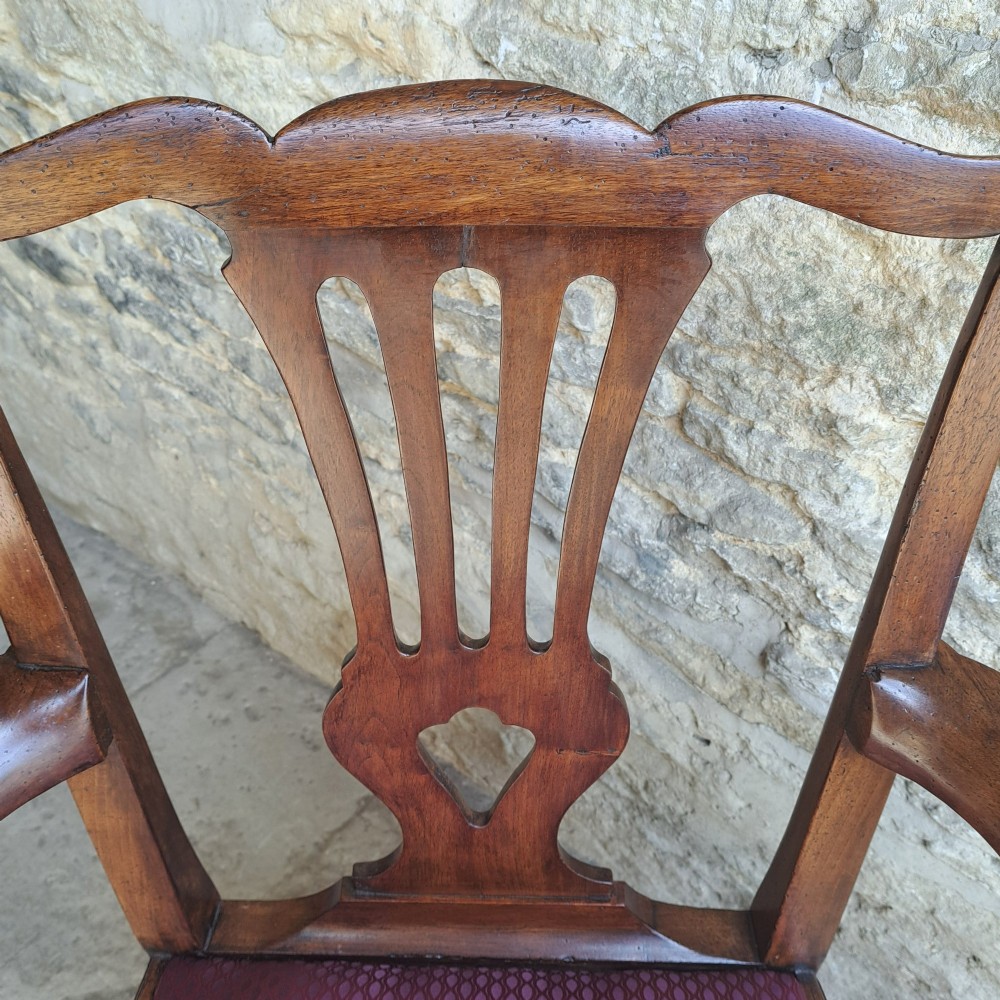 An 18th-century Irish walnut open armchair featuring a carved pierced splat, shaped armrests, an H-stretcher base, and a burgundy pattern upholstered seat. View V