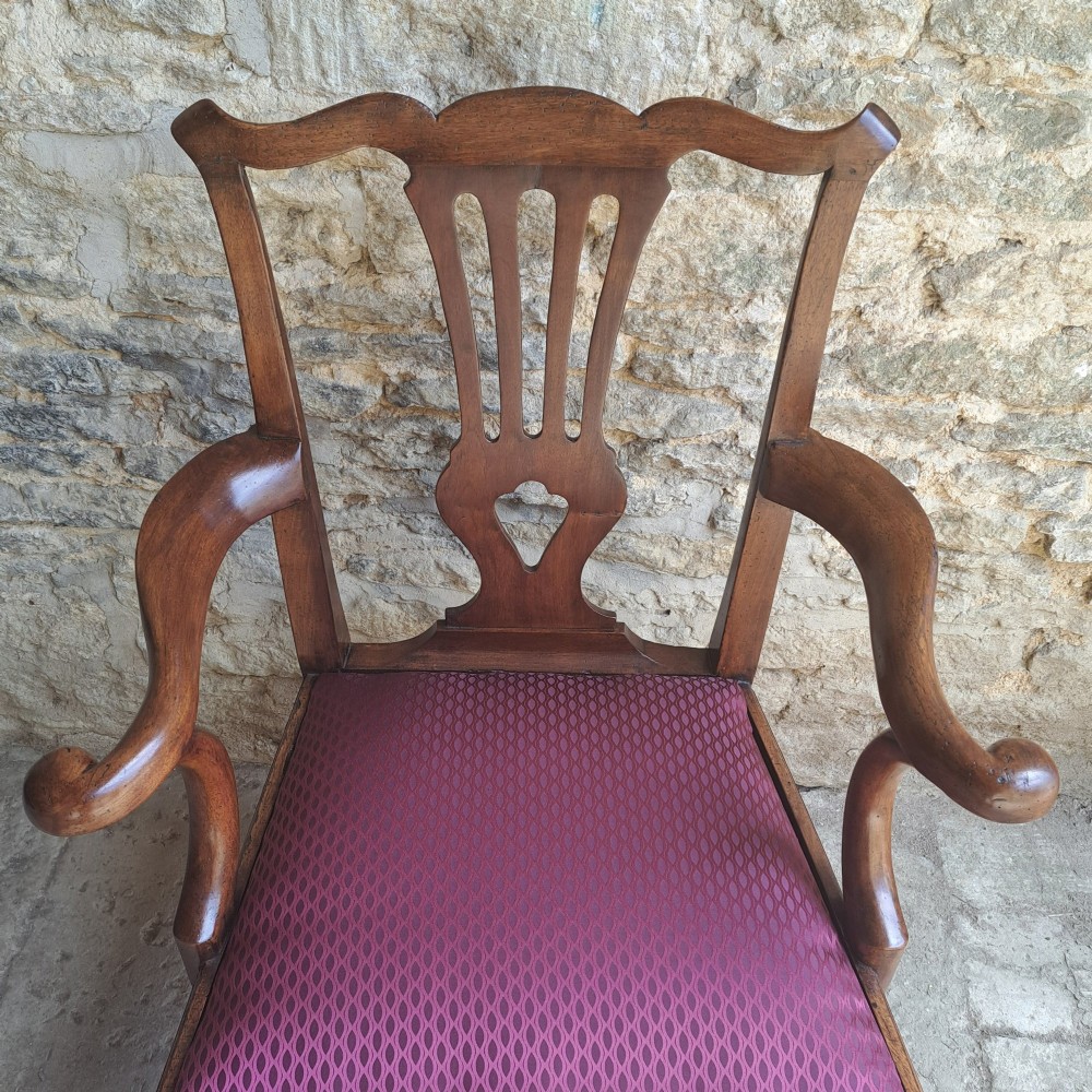 An 18th-century Irish walnut open armchair featuring a carved pierced splat, shaped armrests, an H-stretcher base, and a burgundy pattern upholstered seat. View VI