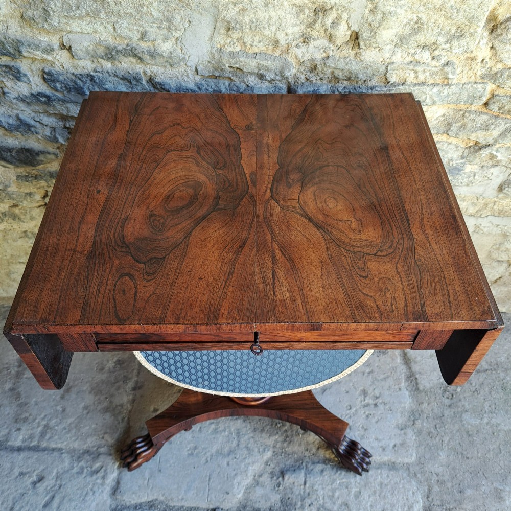 An antique rosewood drop-leaf sewing table with a central drawer, a suspended patterned fabric basket, a turned pedestal column, and carved claw feet. View III