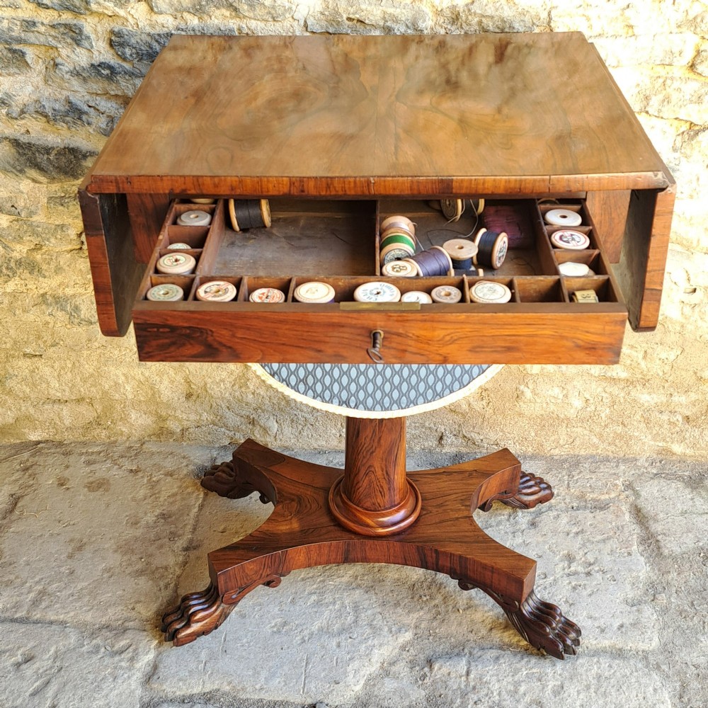 An antique rosewood drop-leaf sewing table with a central drawer, a suspended patterned fabric basket, a turned pedestal column, and carved claw feet. View VII