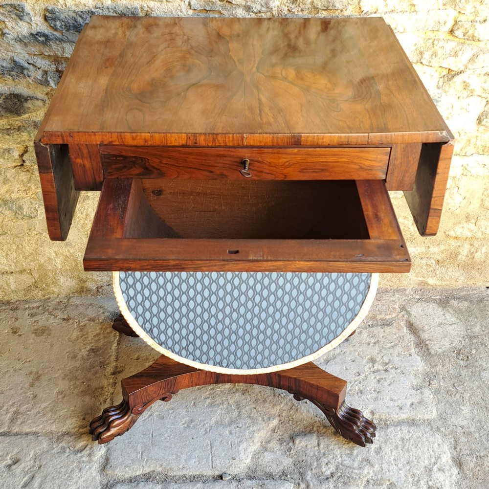 An antique rosewood drop-leaf sewing table with a central drawer, a suspended patterned fabric basket, a turned pedestal column, and carved claw feet. View VIII