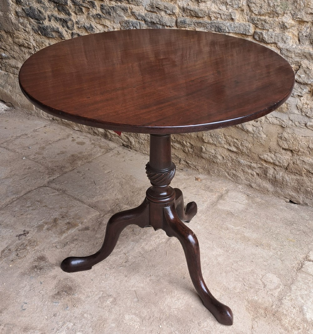 An 18th-century Georgian mahogany tilt-top table featuring a circular top, turned central column with a spirally carved knop, and three cabriole legs ending in pad feet.