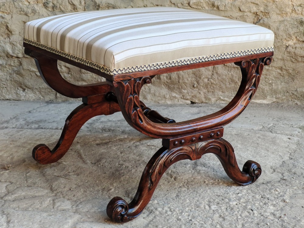 A Regency rosewood X-frame stool featuring intricately carved acanthus leaf scroll legs, a turned central stretcher, and a striped upholstered seat. View II