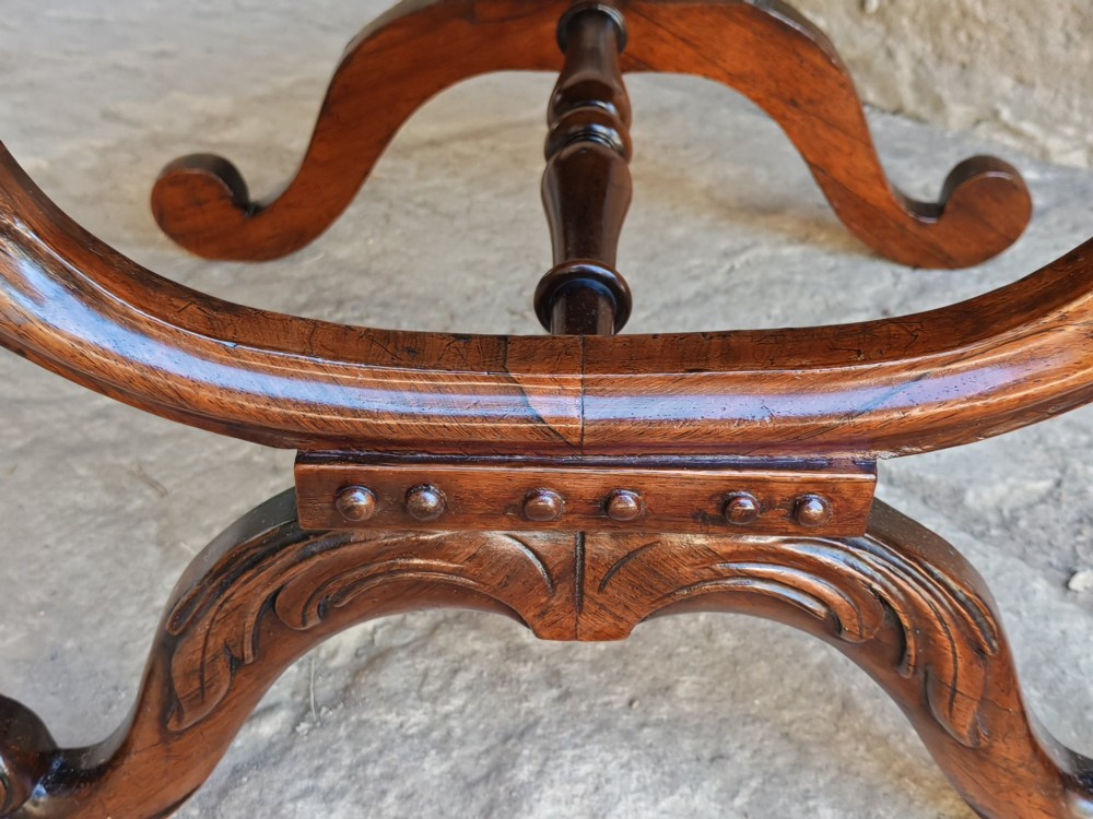A Regency rosewood X-frame stool featuring intricately carved acanthus leaf scroll legs, a turned central stretcher, and a striped upholstered seat. View IV