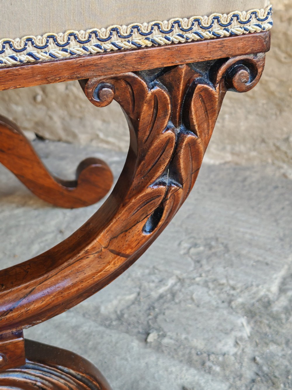A Regency rosewood X-frame stool featuring intricately carved acanthus leaf scroll legs, a turned central stretcher, and a striped upholstered seat. View V