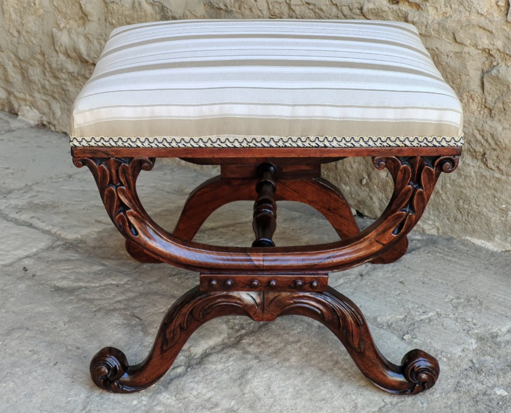 A Regency rosewood X-frame stool featuring intricately carved acanthus leaf scroll legs, a turned central stretcher, and a striped upholstered seat. View VII