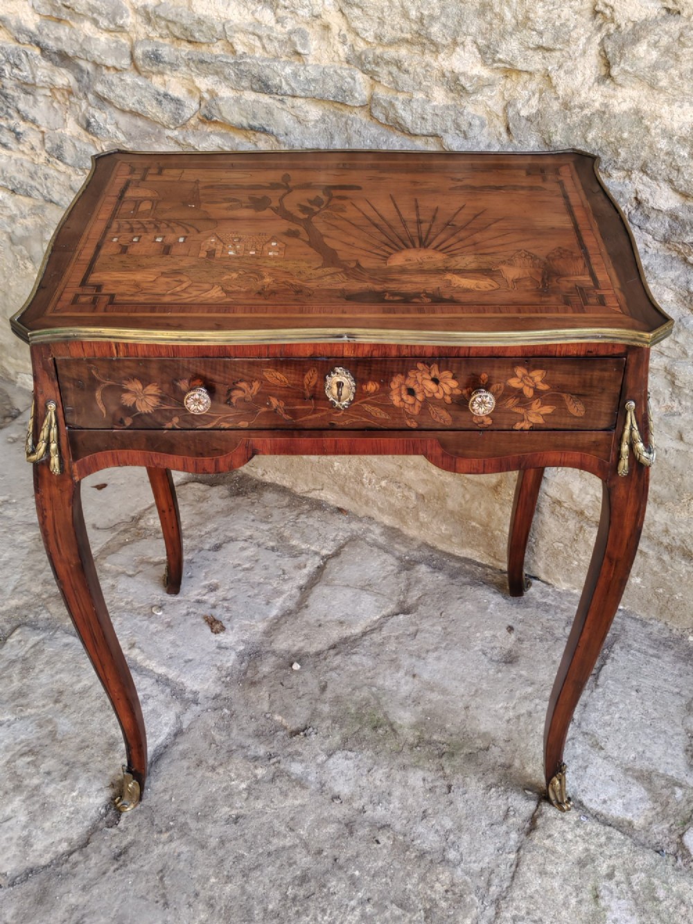 An 18th-century Dutch marquetry side table featuring a pictorial inlaid tabletop depicting a landscape, a floral drawer front, cabriole legs, and brass mounts.