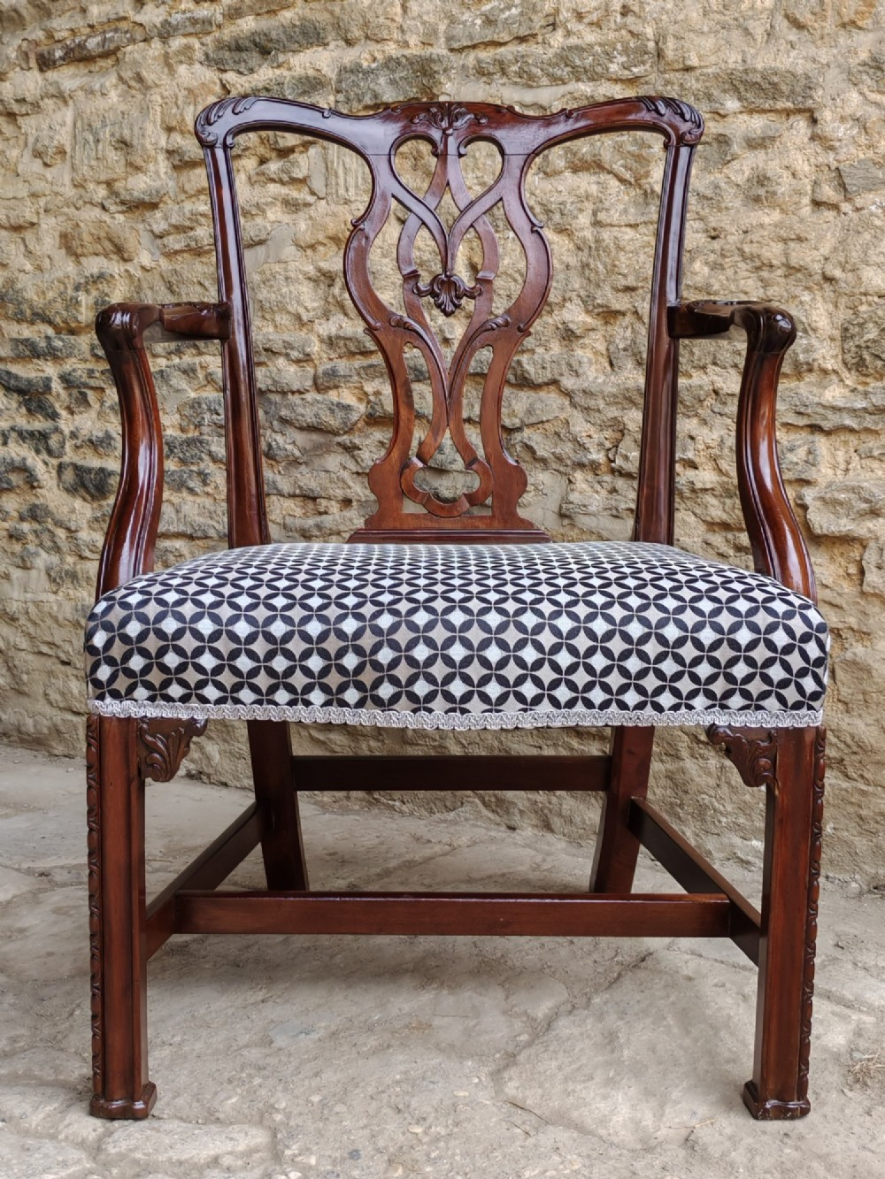 A Georgian mahogany carver armchair featuring a pierced back splat, shaped arms, square carved front legs, and geometric patterned fabric seating.