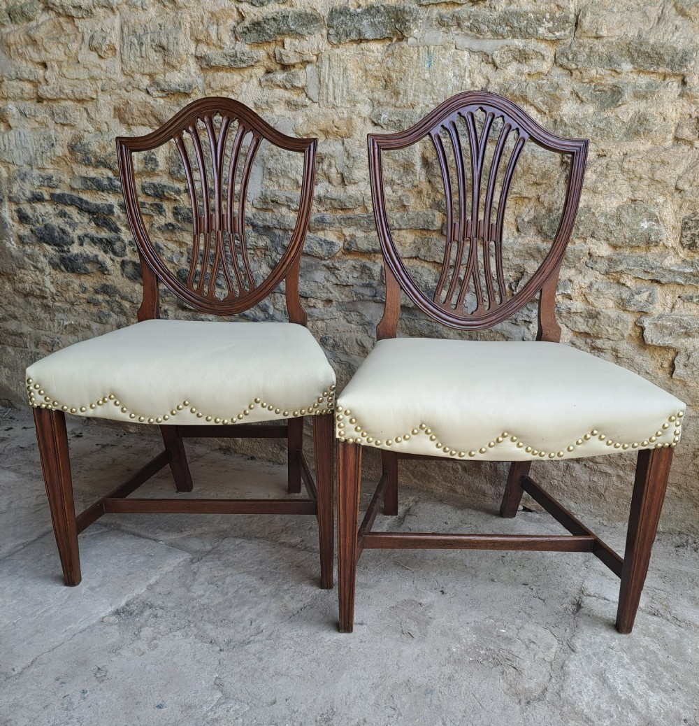 A pair of late 18th-century mahogany Hepplewhite dining chairs featuring carved shield backs and cream leather seats with brass stud detailing. View II