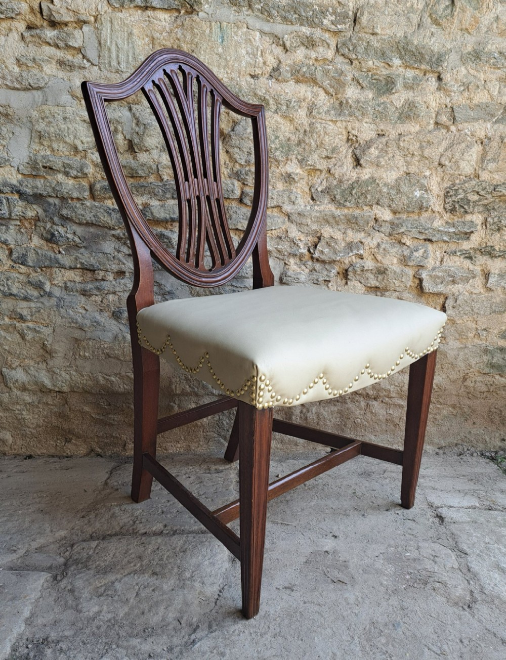 A pair of late 18th-century mahogany Hepplewhite dining chairs featuring carved shield backs and cream leather seats with brass stud detailing. View III