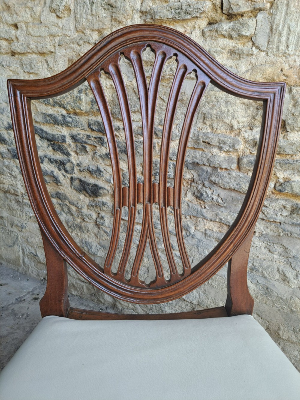 A pair of late 18th-century mahogany Hepplewhite dining chairs featuring carved shield backs and cream leather seats with brass stud detailing. View IV