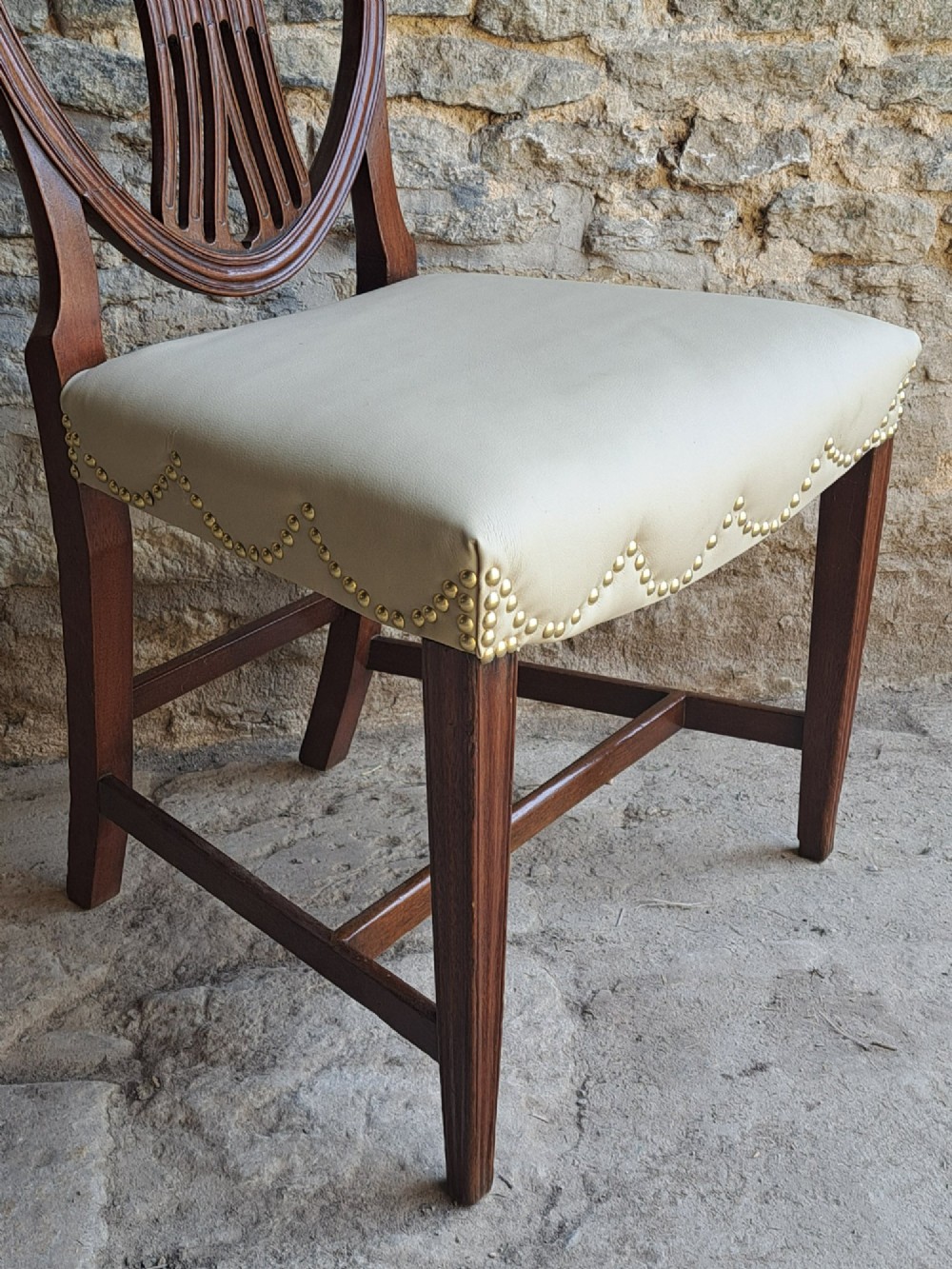 A pair of late 18th-century mahogany Hepplewhite dining chairs featuring carved shield backs and cream leather seats with brass stud detailing. View VII
