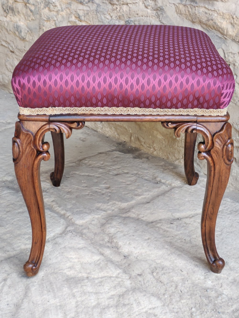 A mid-19th century rosewood stool with carved cabriole legs and a burgundy patterned upholstered seat trimmed with gold braid. View II