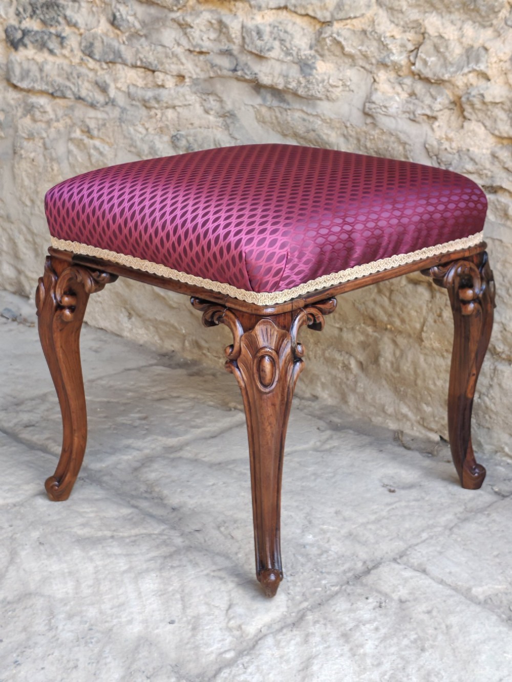 A mid-19th century rosewood stool with carved cabriole legs and a burgundy patterned upholstered seat trimmed with gold braid. View III