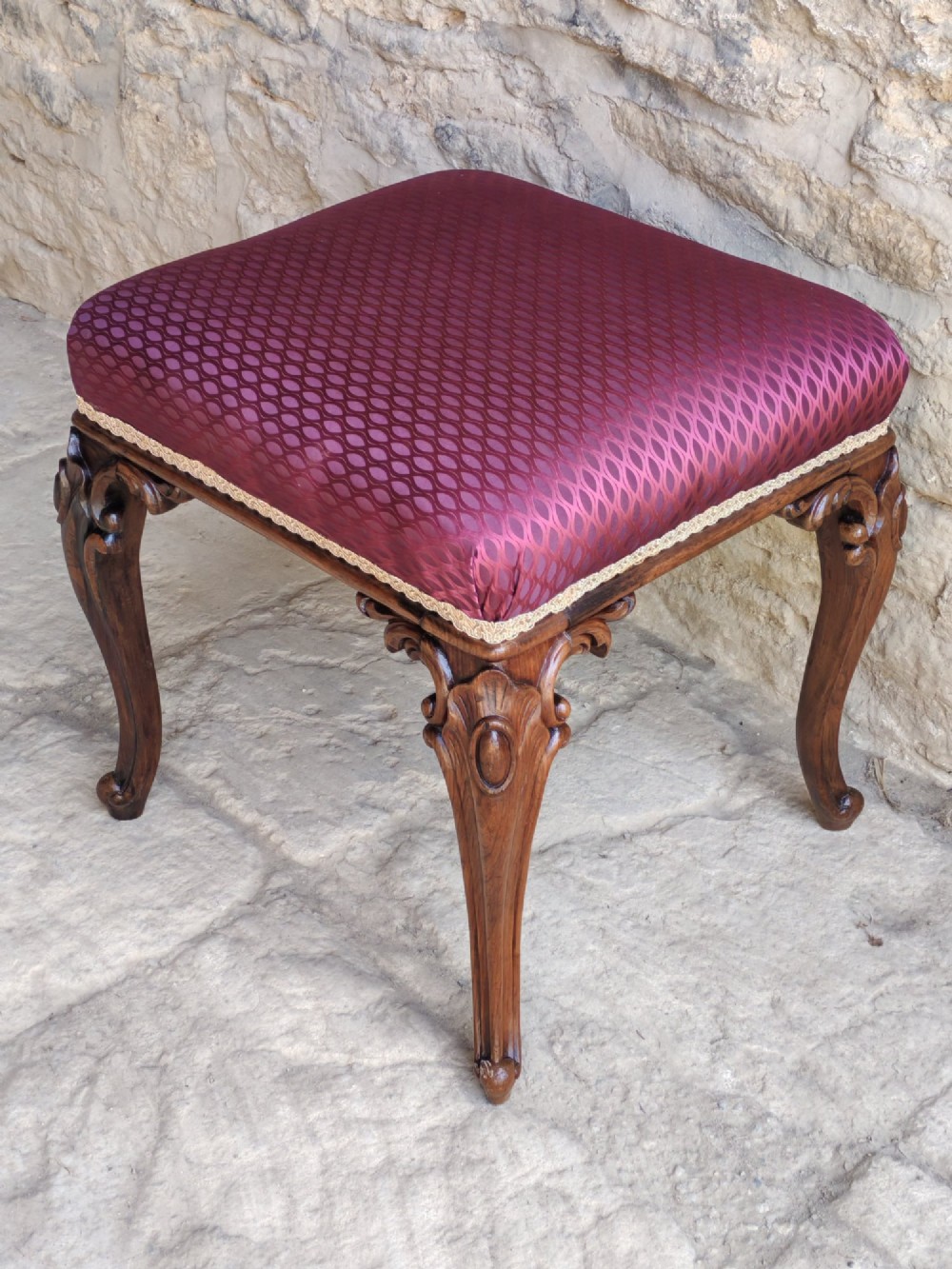 A mid-19th century rosewood stool with carved cabriole legs and a burgundy patterned upholstered seat trimmed with gold braid. View IV