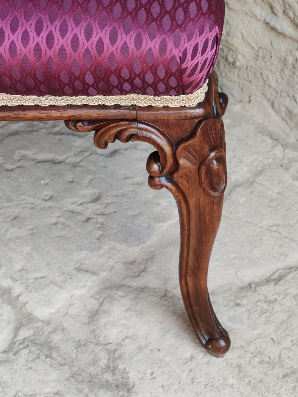 A mid-19th century rosewood stool with carved cabriole legs and a burgundy patterned upholstered seat trimmed with gold braid. View V