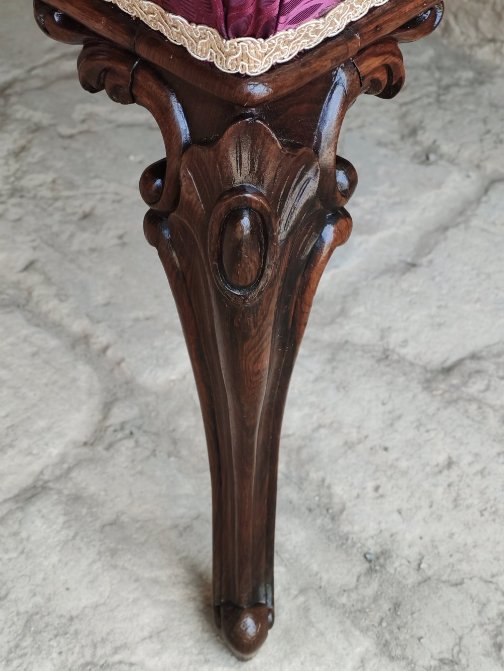 A mid-19th century rosewood stool with carved cabriole legs and a burgundy patterned upholstered seat trimmed with gold braid. View VI
