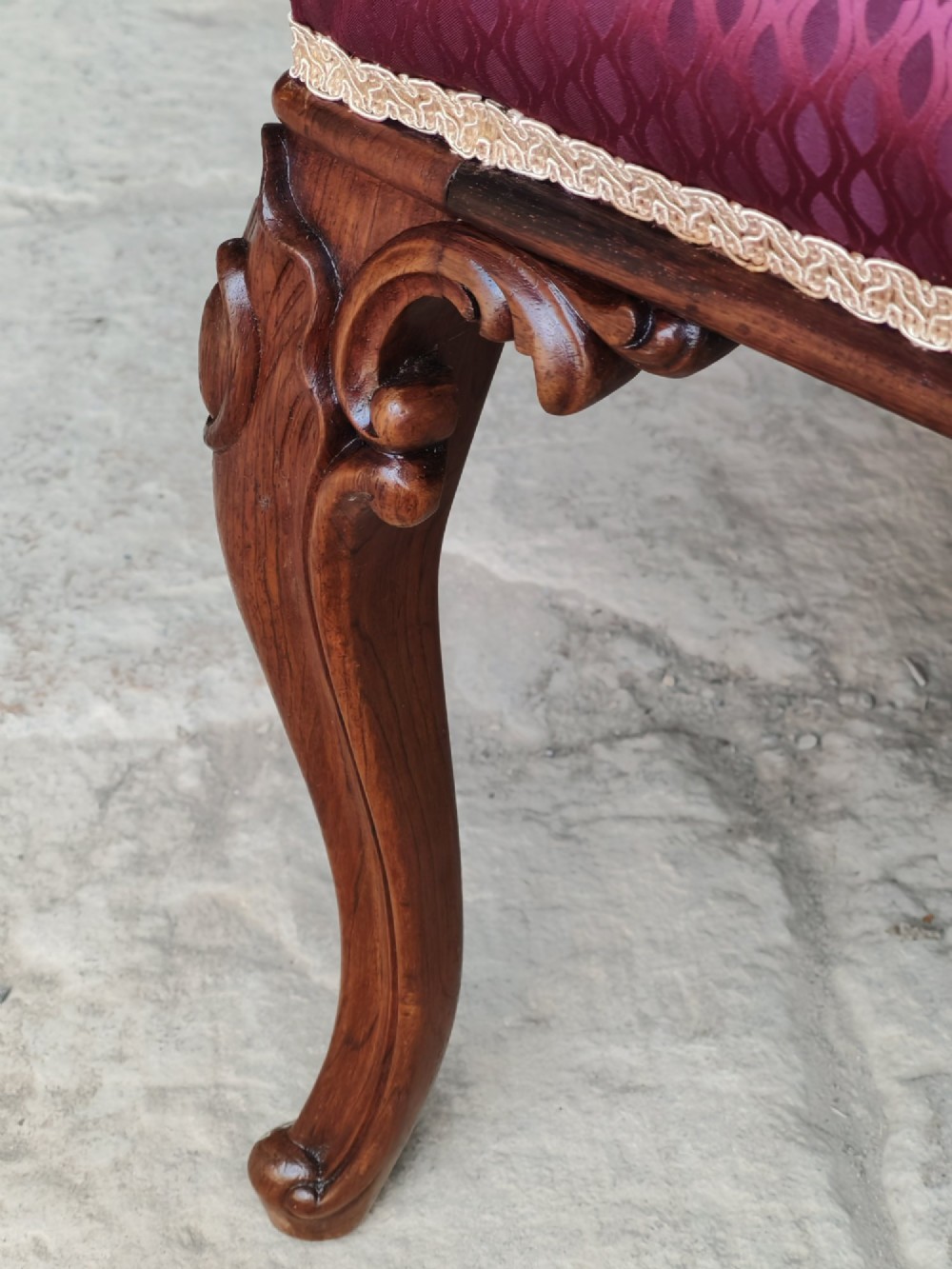 A mid-19th century rosewood stool with carved cabriole legs and a burgundy patterned upholstered seat trimmed with gold braid. View VII