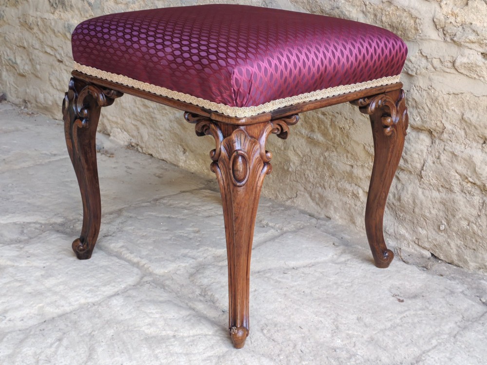 A mid-19th century rosewood stool with carved cabriole legs and a burgundy patterned upholstered seat trimmed with gold braid.