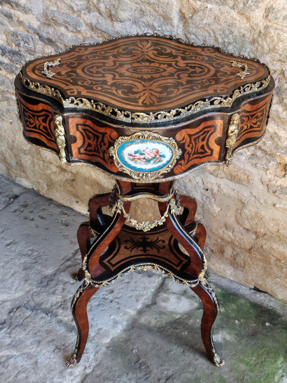 A 19th-century French marquetry jardiniere table with intricate wood inlay, ornate gilded mounts, a cherub porcelain plaque, and cabriole legs.