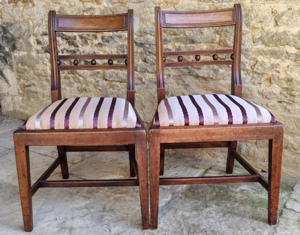 A pair of antique mahogany side chairs featuring reeded frames, a ball-ornamented mid-rail, and striped upholstered seats.