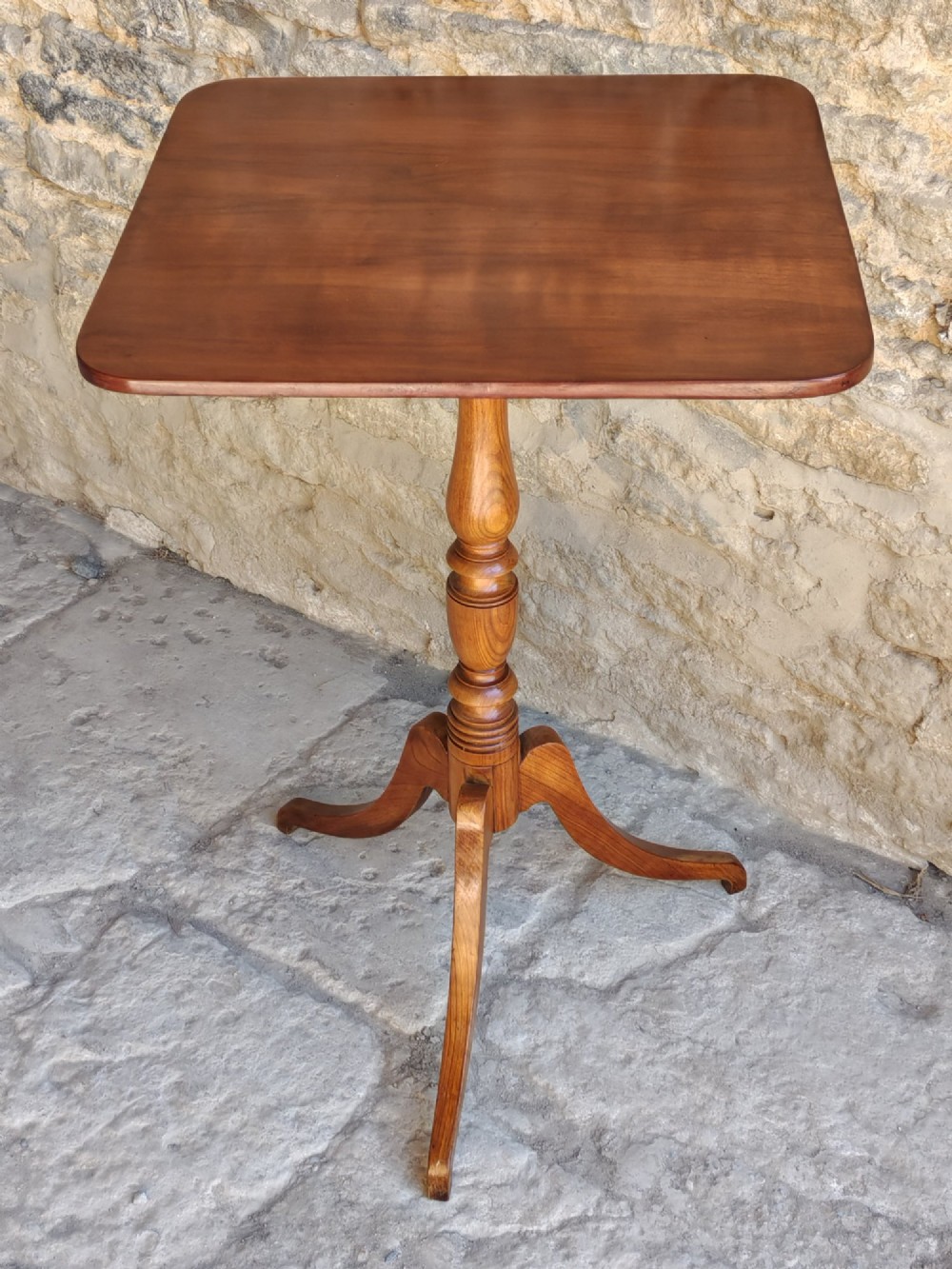 A square top antique fruitwood wine table featuring rounded corners, a central turned baluster stem, and three splayed tripod legs.