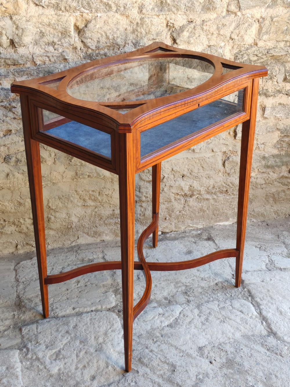 A late Victorian satinwood bijouterie table featuring an oval glazed top aperture, glass side panels, tapered square legs, and an X-form stretcher. View II
