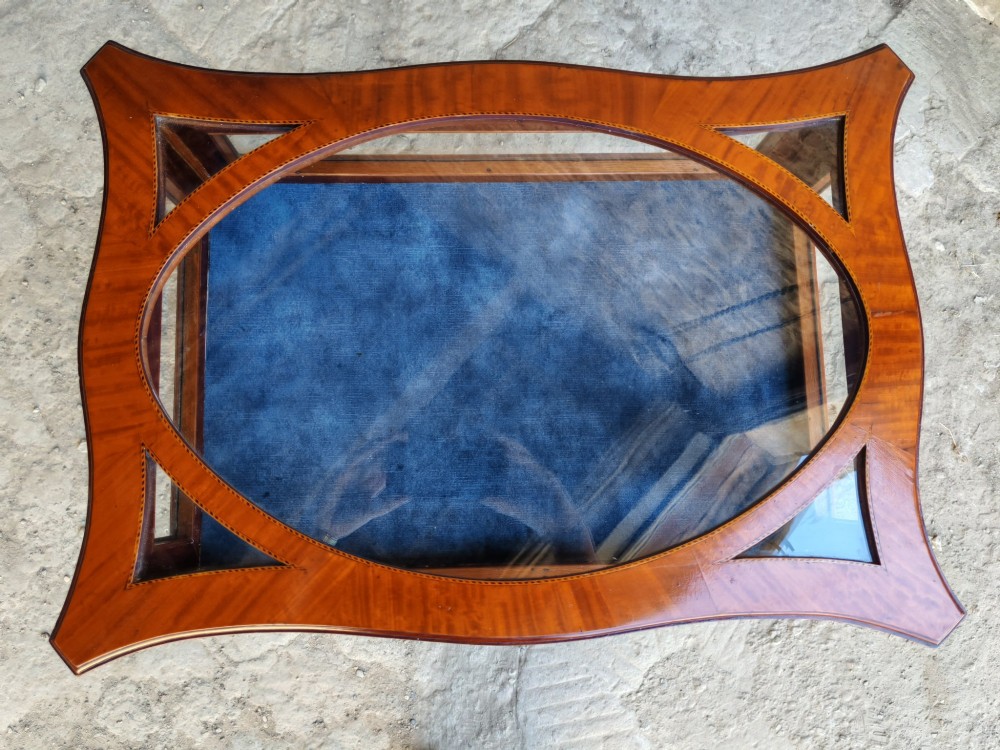 A late Victorian satinwood bijouterie table featuring an oval glazed top aperture, glass side panels, tapered square legs, and an X-form stretcher. View V