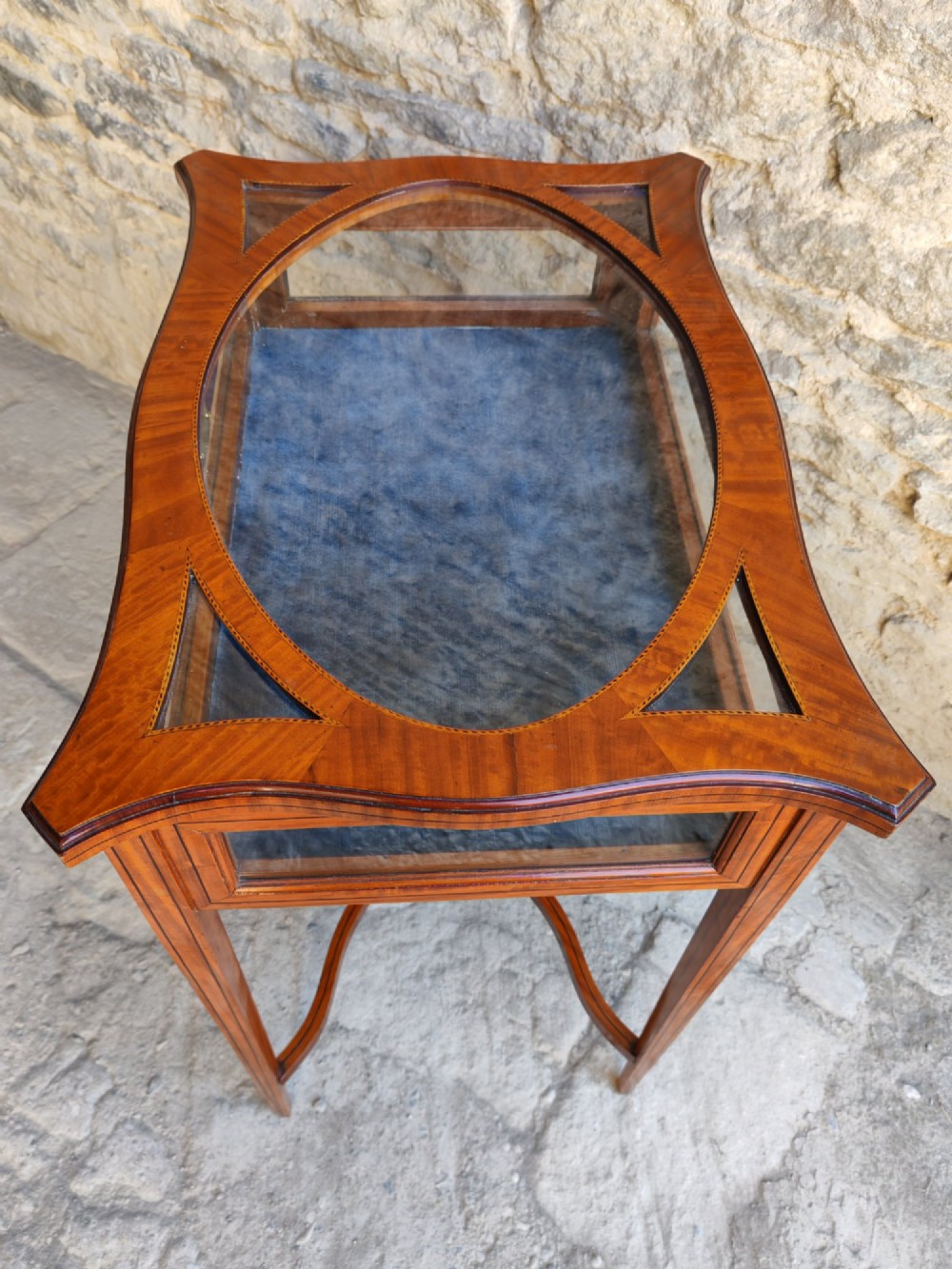 A late Victorian satinwood bijouterie table featuring an oval glazed top aperture, glass side panels, tapered square legs, and an X-form stretcher. View IX