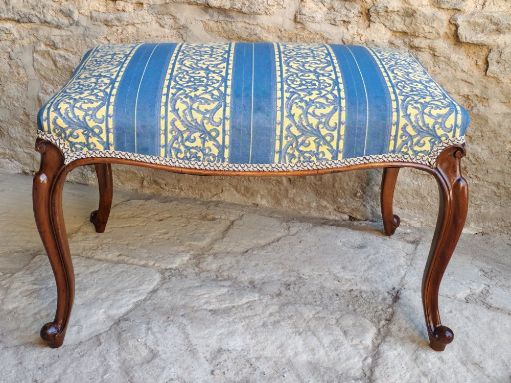 An antique walnut stool featuring carved cabriole legs and a patterned blue and yellow striped upholstered top with gimp trim.