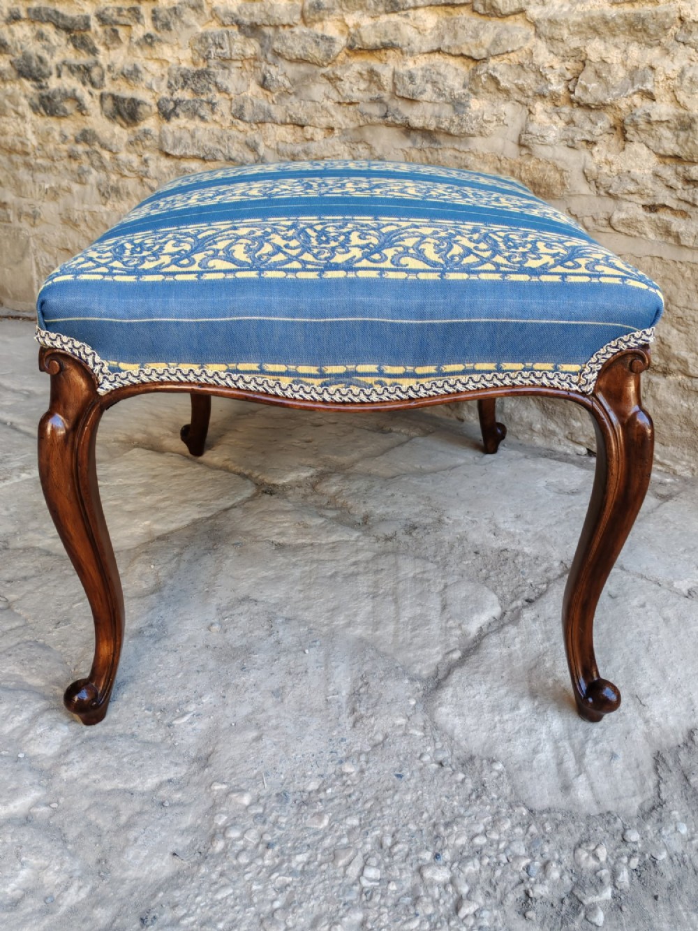An antique walnut stool featuring carved cabriole legs and a patterned blue and yellow striped upholstered top with gimp trim. View V