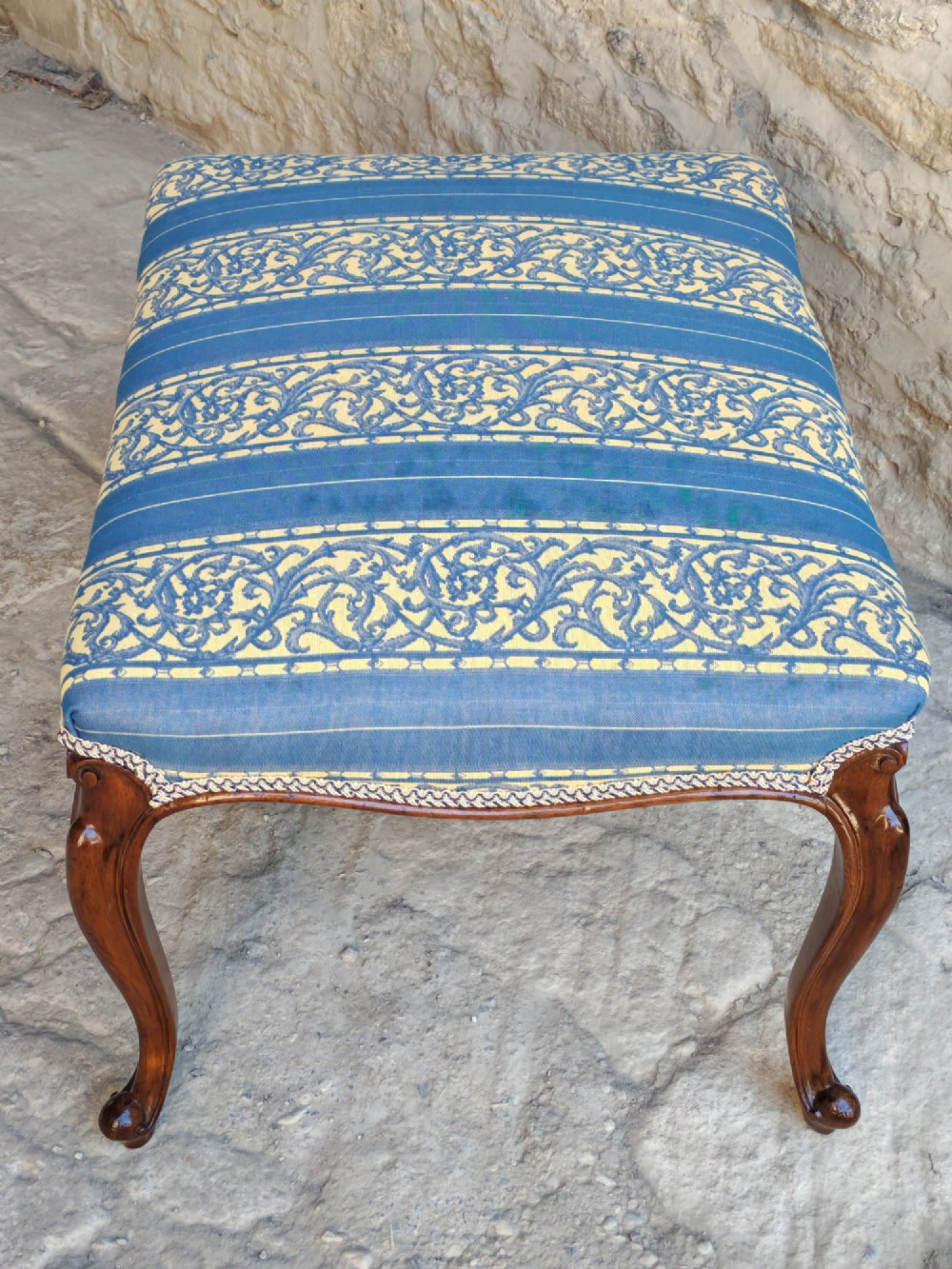 An antique walnut stool featuring carved cabriole legs and a patterned blue and yellow striped upholstered top with gimp trim. View VI