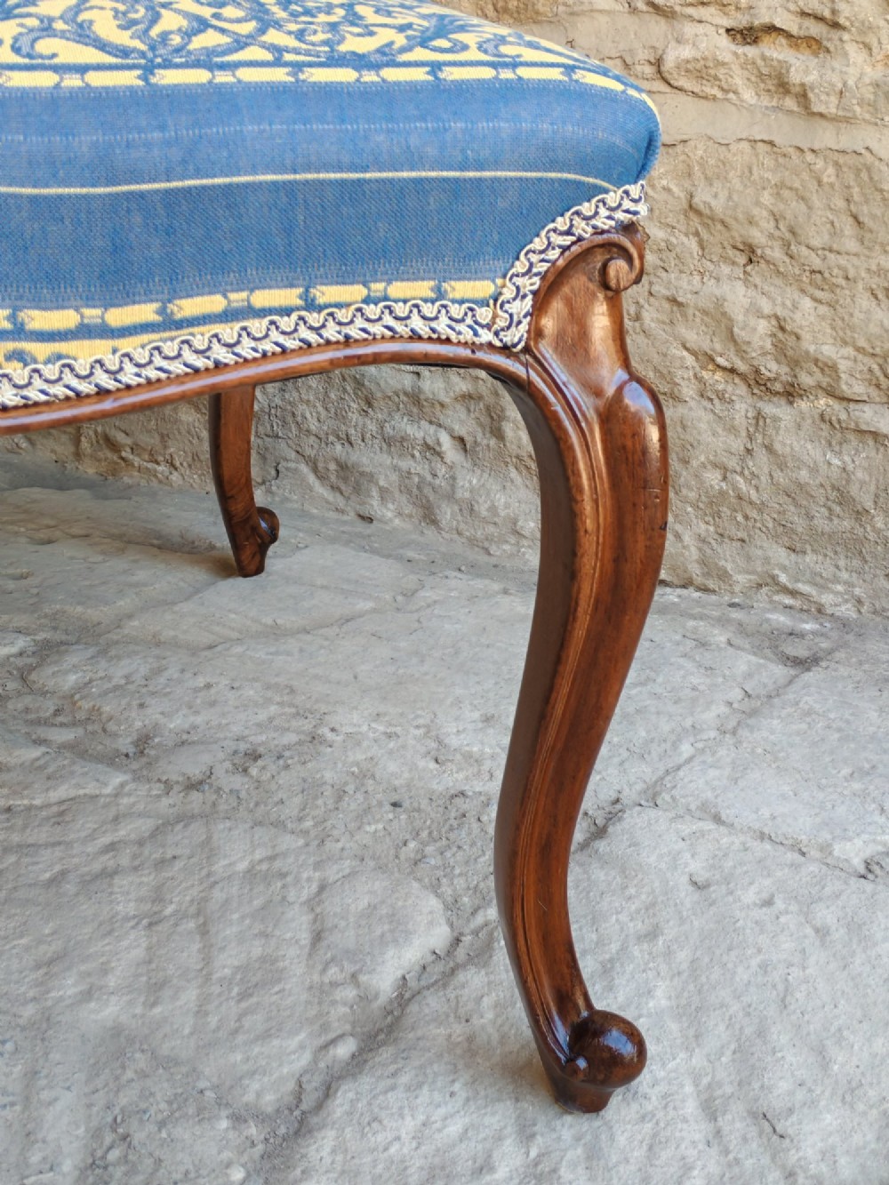 An antique walnut stool featuring carved cabriole legs and a patterned blue and yellow striped upholstered top with gimp trim. View VII