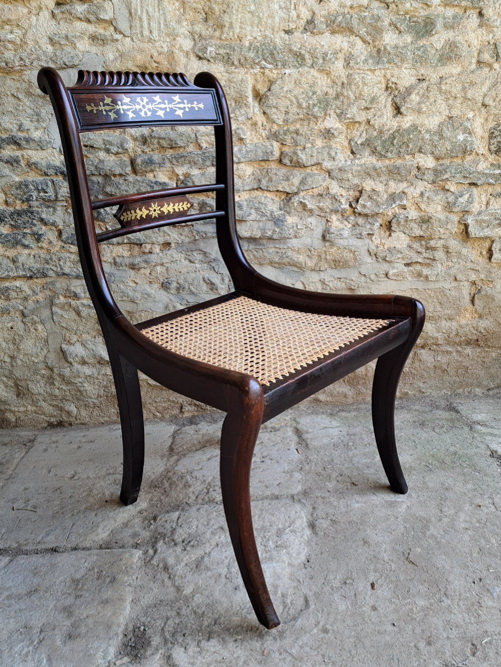 A set of four dark rosewood Regency dining chairs featuring intricate brass inlaid backrails, carved crests, hand-woven cane seats, and curved sabre legs. View IV