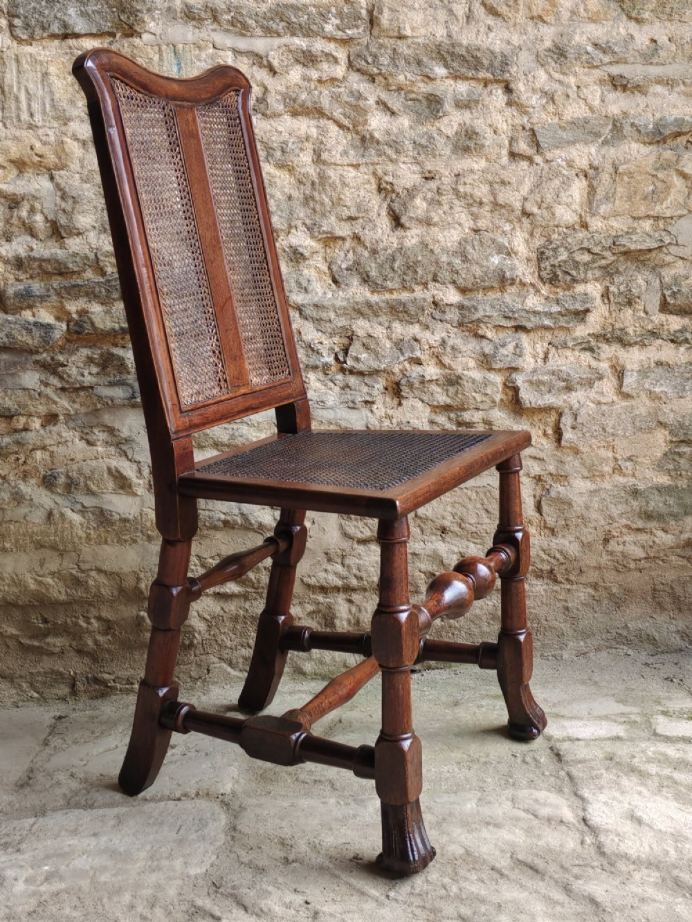 An early 18th-century dark walnut side chair featuring a high back with woven cane panels and central wooden splat, a caned seat, and turned legs with carved feet. View II