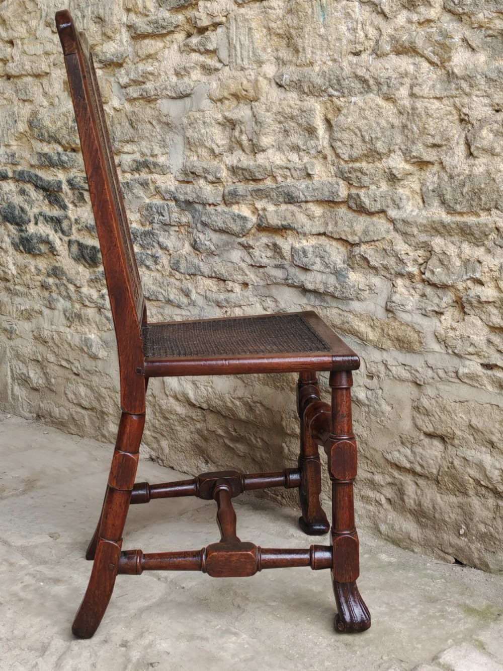 An early 18th-century dark walnut side chair featuring a high back with woven cane panels and central wooden splat, a caned seat, and turned legs with carved feet. View III