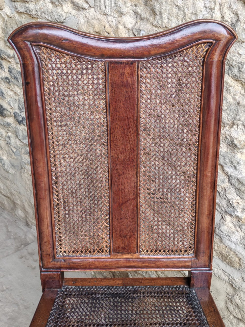 An early 18th-century dark walnut side chair featuring a high back with woven cane panels and central wooden splat, a caned seat, and turned legs with carved feet. View V