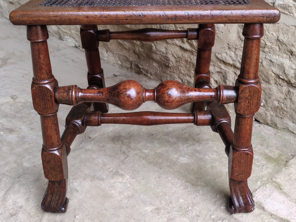 An early 18th-century dark walnut side chair featuring a high back with woven cane panels and central wooden splat, a caned seat, and turned legs with carved feet. View VII