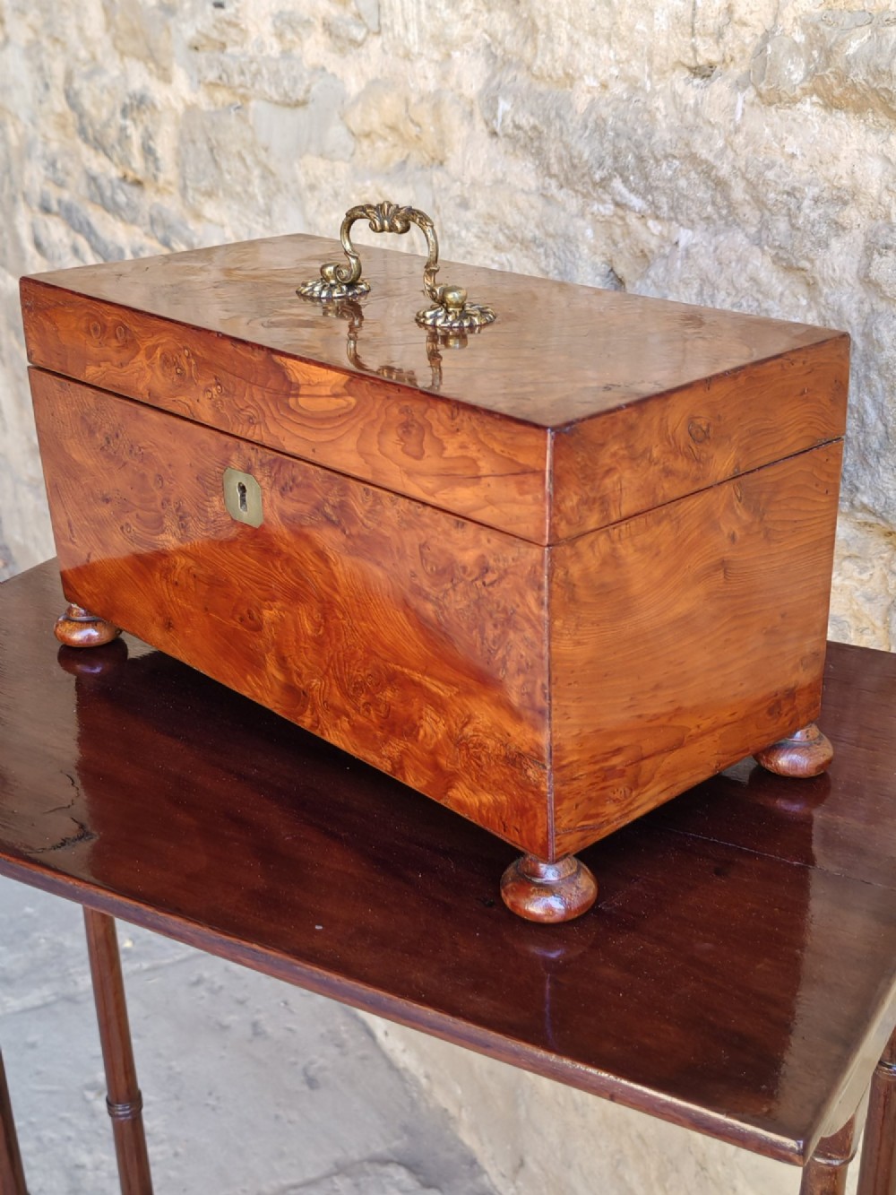An 18th-century Georgian yew wood tea caddy featuring rich grain figure, a top brass handle, a brass escutcheon, and bun feet. View II