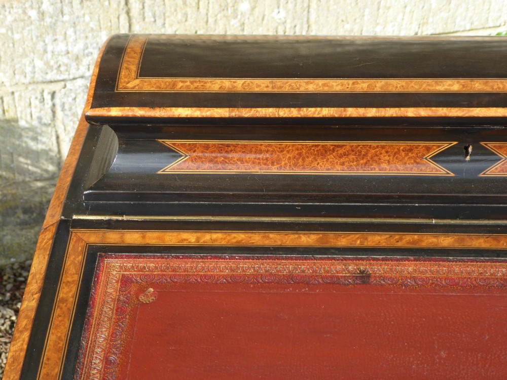 A Victorian ebonised and amboyna Davenport desk featuring a slanted leather-lined writing surface above a side cabinet door opening to reveal internal drawers. View VI