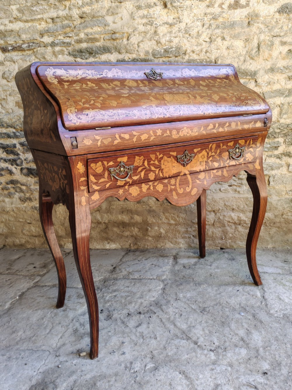 An antique Dutch walnut cylinder bureau decorated with floral marquetry inlays, resting on slender cabriole legs. View II