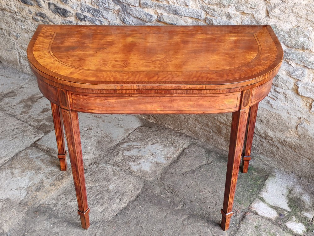 A late 18th-century D-shaped satinwood card table with fine crossbanding, stringing inlay, and square tapered legs.