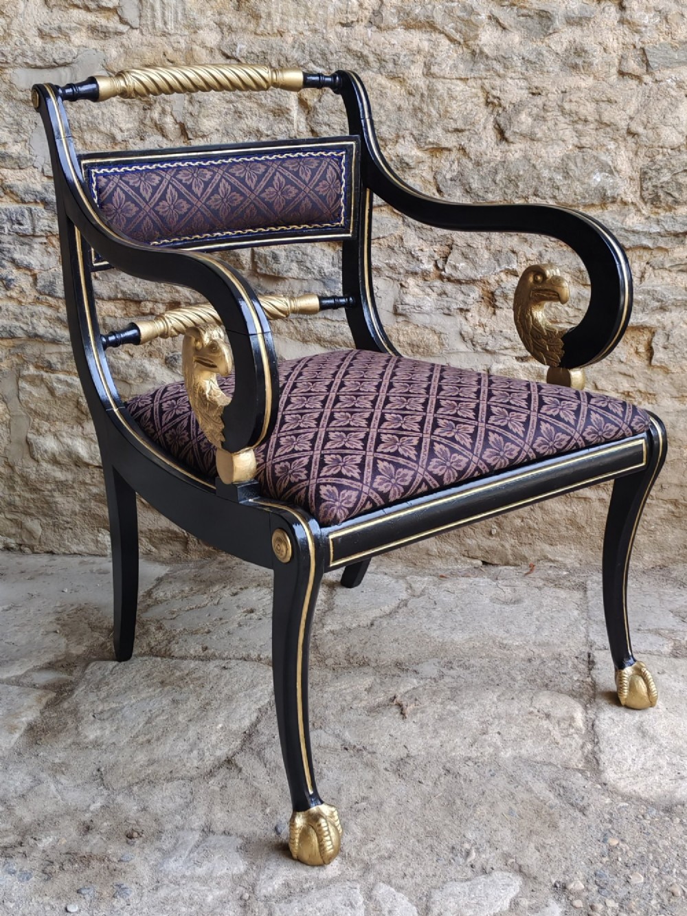 An ebonised and parcel-gilt Regency armchair featuring carved eagle head arm terminals, reeded scroll bars, patterned purple fabric upholstery, and gold paw feet. View II