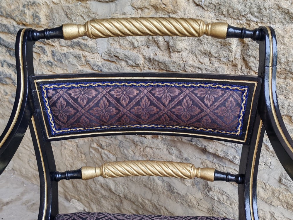 An ebonised and parcel-gilt Regency armchair featuring carved eagle head arm terminals, reeded scroll bars, patterned purple fabric upholstery, and gold paw feet. View IV