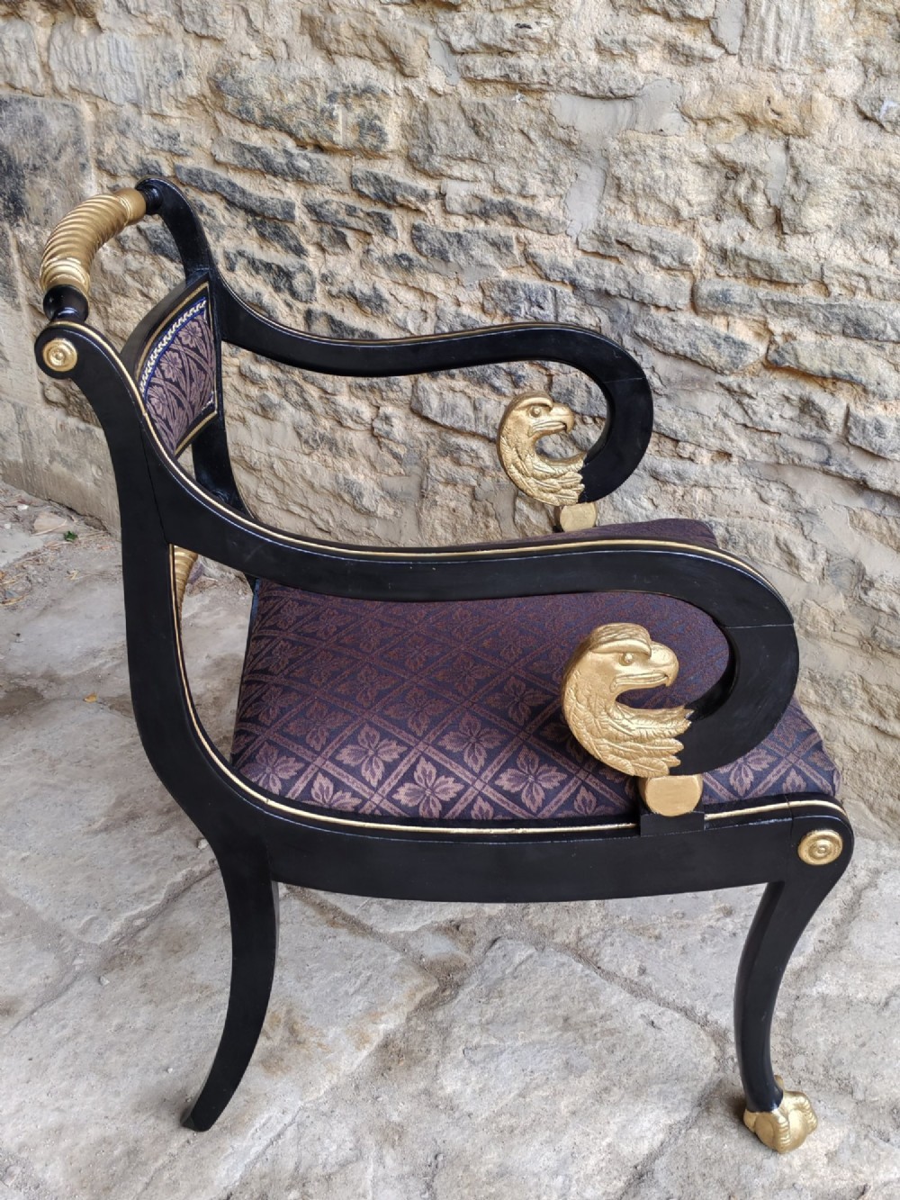 An ebonised and parcel-gilt Regency armchair featuring carved eagle head arm terminals, reeded scroll bars, patterned purple fabric upholstery, and gold paw feet. View V